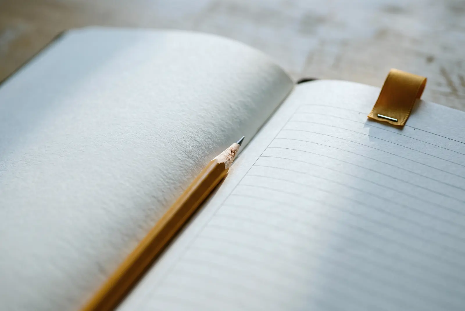 Açık duran boş çizgili bir defter, ortasında bir kurşun kalem ve sayfa kenarında amber bir ayraç.